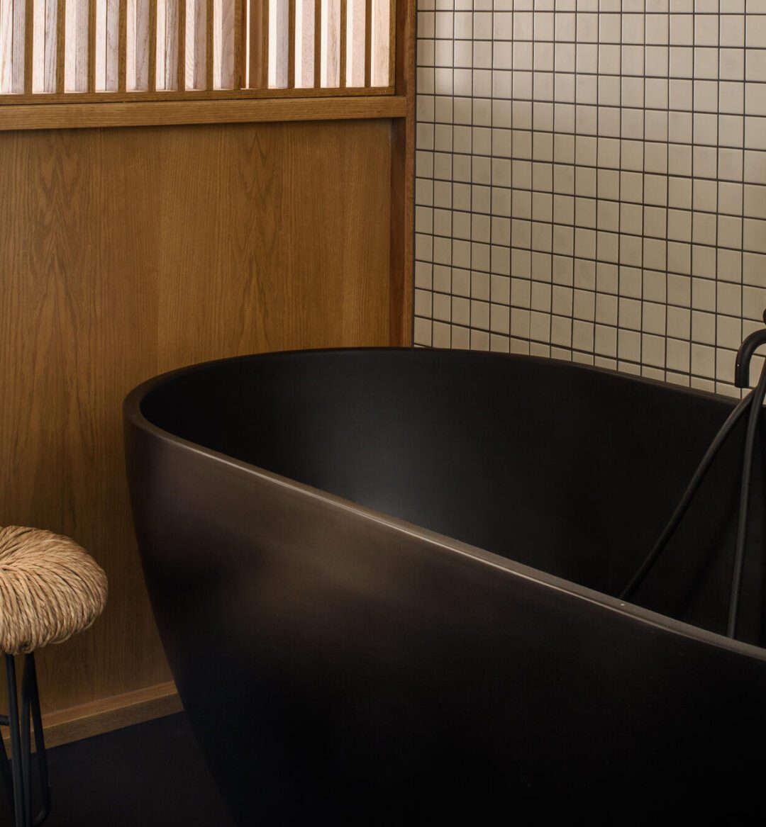 A sleek black bathtub in a stylish bathroom, accompanied by a wooden stool nearby.