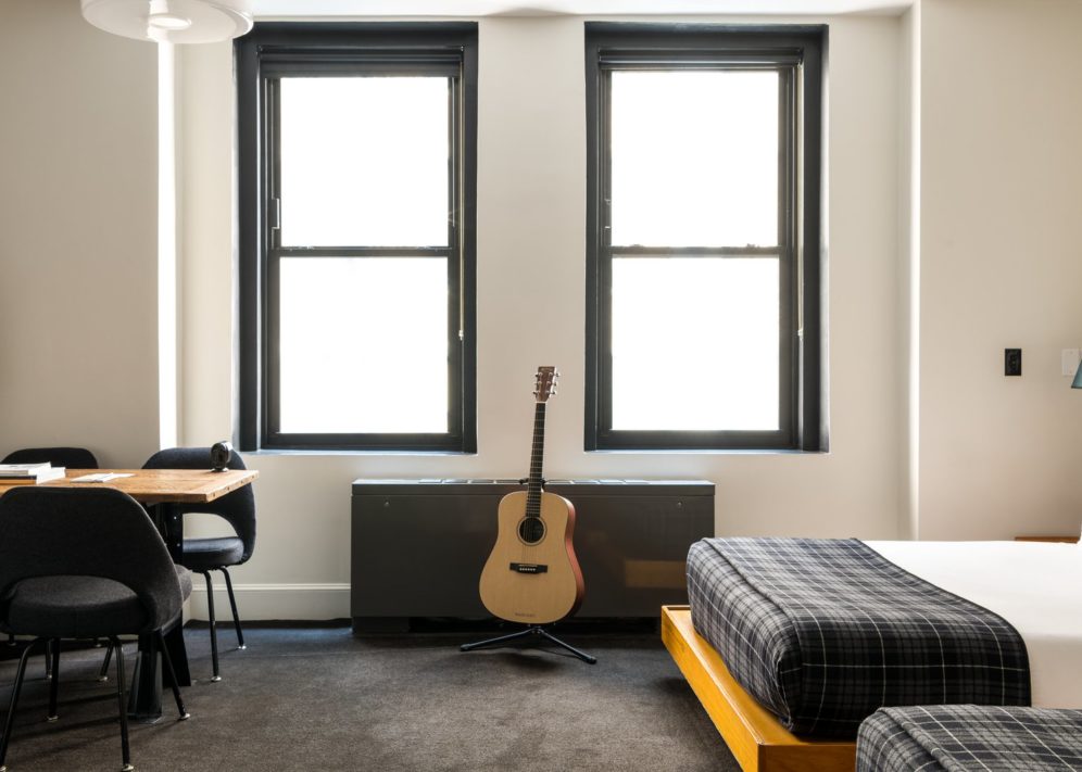 A room with dark carpets features 2 windows and a corner desk with multiple chairs