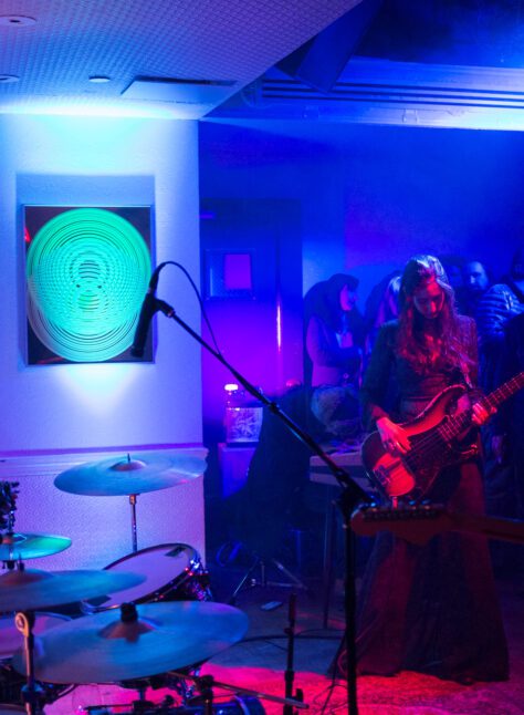woman playing guitar in blue and red lit event venue next to drumset for private music event at Ace Hotel NY.