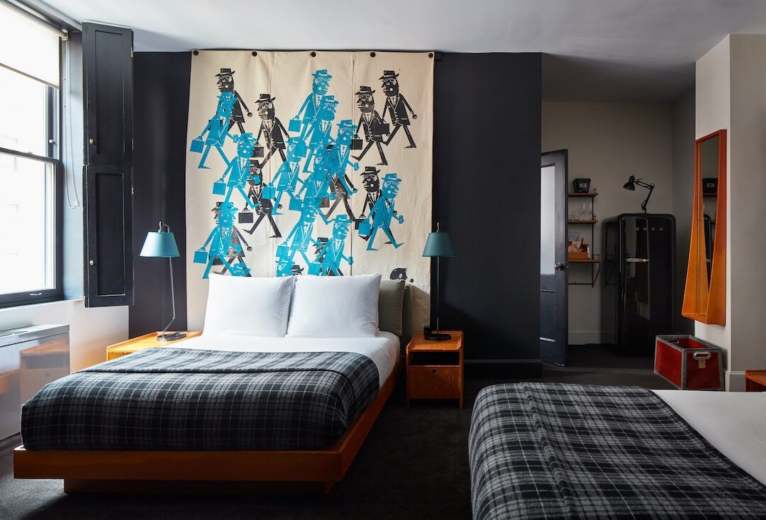 Two neatly made beds with a partition in the back with silk screened image.