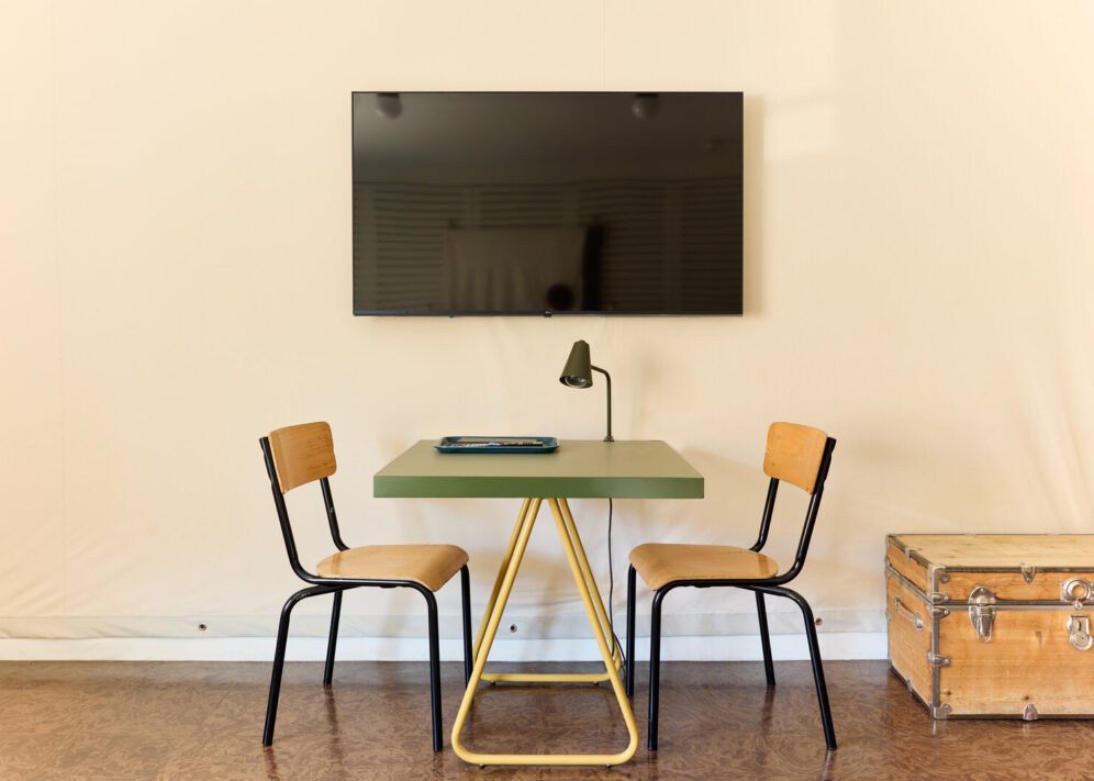 A simple green desk with a reading lamp sits under a television