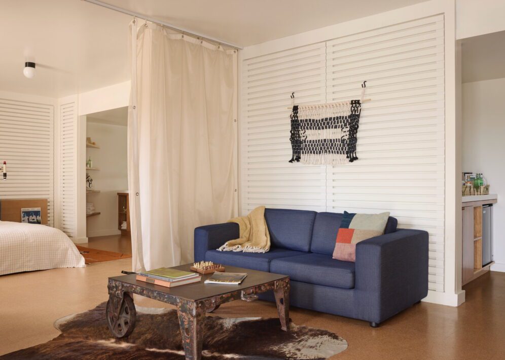 A blue sofa and rustic coffee table provide a place to sit and relax; a curtain separate the living room from the bedroom