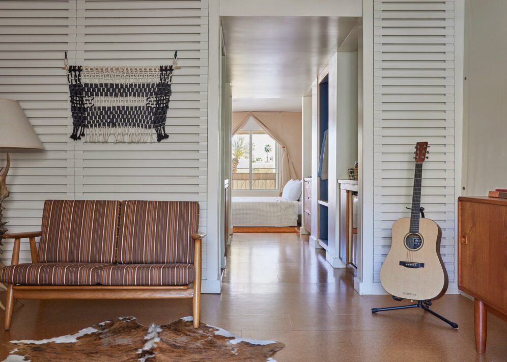 A small couch sits in front of an animal skin rug; a hallway leads to a bedroom with natural light