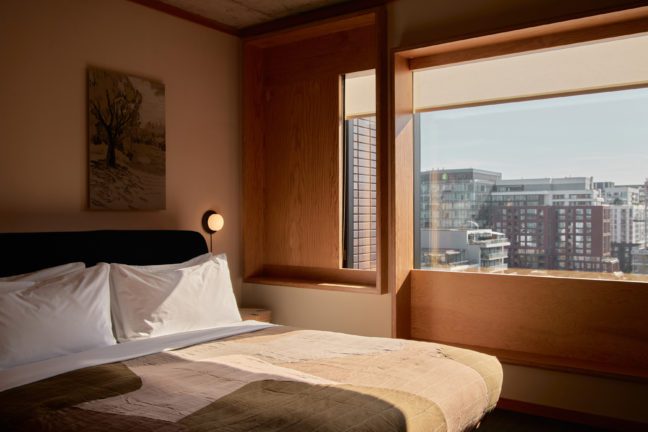 A bed sits next to two windows, offering expansive views of the city