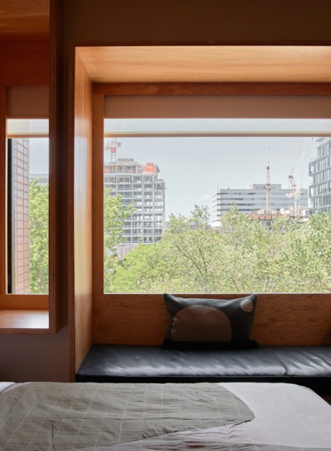 A wood paneled room features a black leather seating area under a window featuring greenery